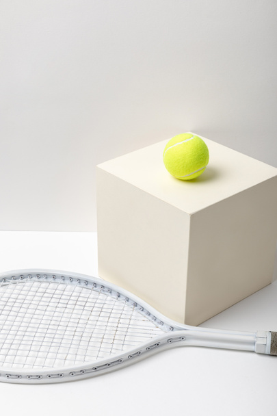tennis racket and bright yellow tennis ball on cube on white background - Foto, imagen
