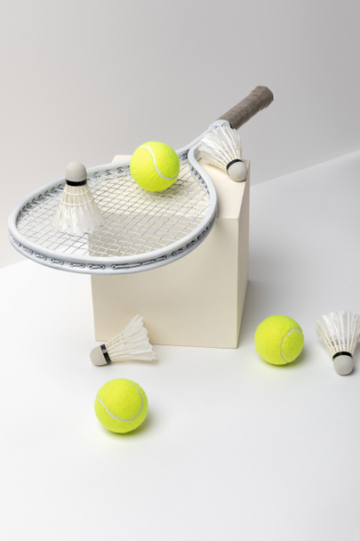 白い背景に立方体にシャトルコックとテニスラケットと明るい黄色のテニスボール - 写真・画像