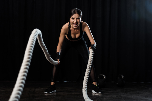 selective focus of sportswoman exercising with battle ropes on black  - Fotoğraf, Görsel