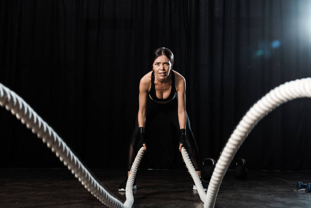 selective focus of woman exercising with battle ropes on black  - Photo, Image