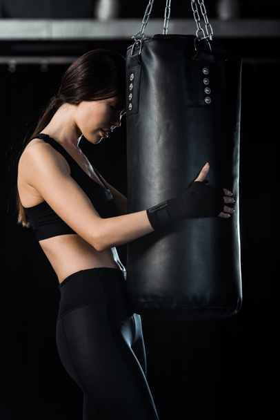 attractive girl standing and holding punching bag on black  - Photo, Image