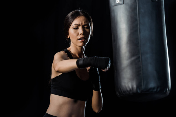 selective focus of attractive girl working out near punching bag isolated on black  - Foto, afbeelding