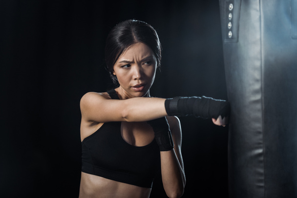 selective focus of girl working out near punching bag isolated on black  - Foto, Bild