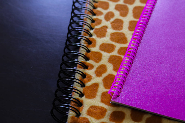 上から見た黒い背景を持つヒョウ柄のノートとピンクのノートのディテール、オフィスオブジェクト - 写真・画像
