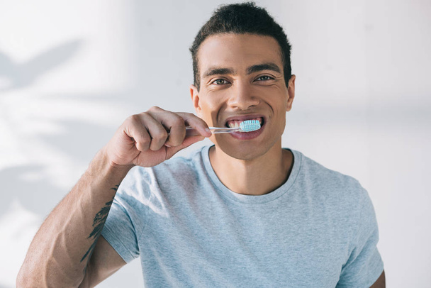 jeune homme brossant les dents avec une brosse à dents et regardant la caméra
 - Photo, image