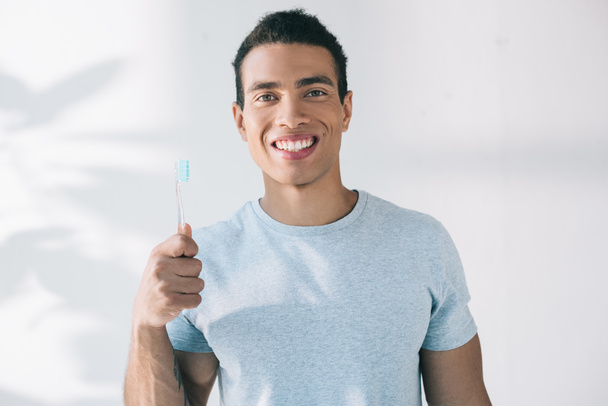 handsome young man holding toothbrush, smiling and looking at camera - Valokuva, kuva