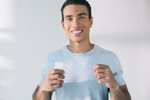 handsome young man holding dental floss while and looking at camera - Foto, afbeelding