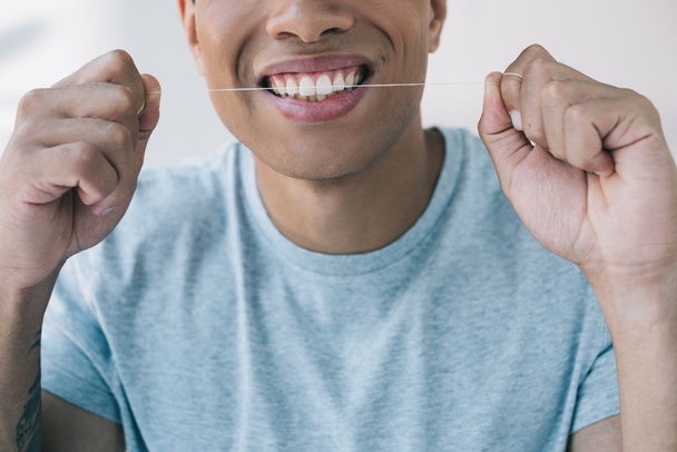cropped view of young man smiling and using dental floss - 写真・画像