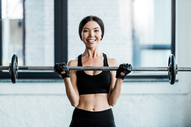 cheerful woman working out with barbell in gym  - Foto, afbeelding