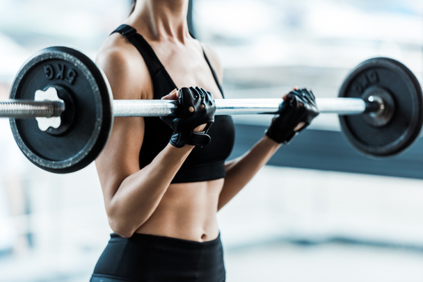 cropped view of young woman in sportswear exercising with barbell in gym  - Foto, immagini