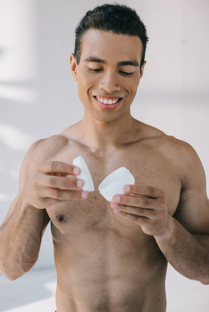 handsome mixed race man opening container with cosmetic cream - Foto, imagen