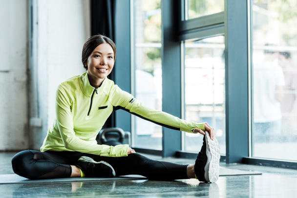 cheerful young woman stretching on fitness mat in gym  - Photo, Image