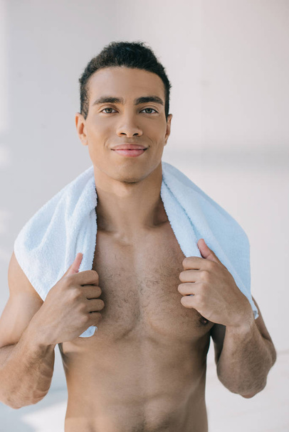 muscular mixed race man holding blue towel on shoulders and looking at camera - Photo, Image
