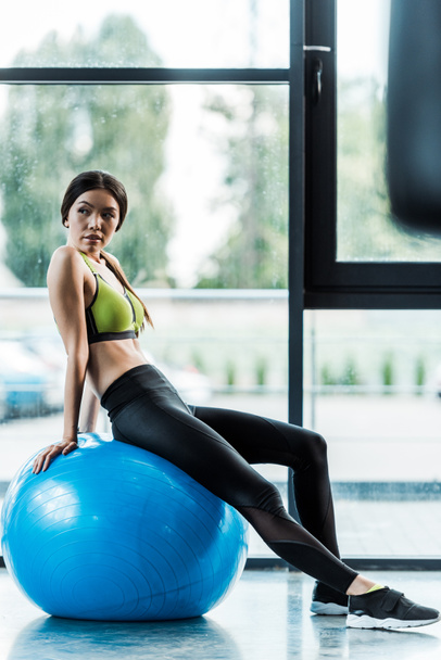 selective focus of beautiful girl sitting on blue fitness ball near dumbbells  - Photo, Image
