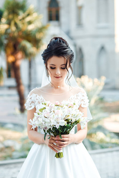 Bride with a wedding bouquet of white flowers in the hands on the background of the castle. - Zdjęcie, obraz