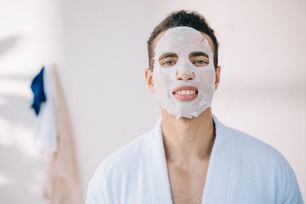 young man in bathrobe with face mask looking at camera - Foto, afbeelding