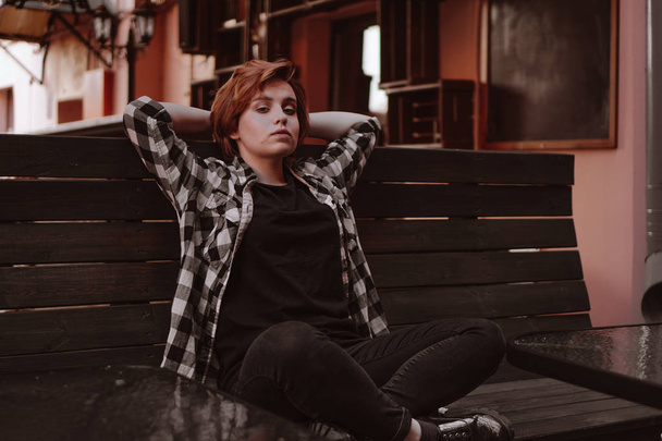 Young woman with short red hair in a bar put her legs on the bench - Φωτογραφία, εικόνα