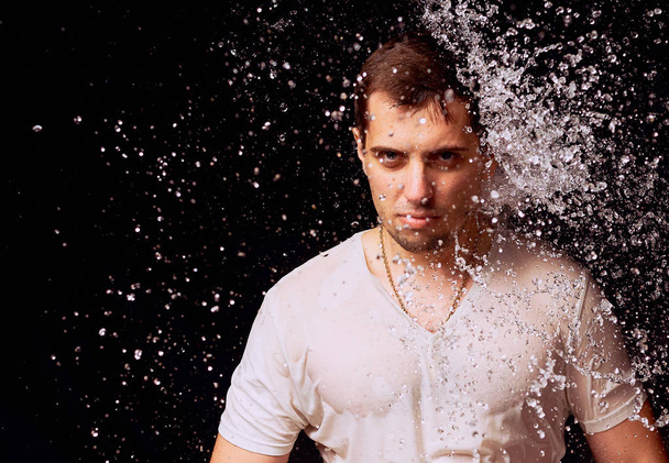 Splashes of water on the young man on dark background - 写真・画像