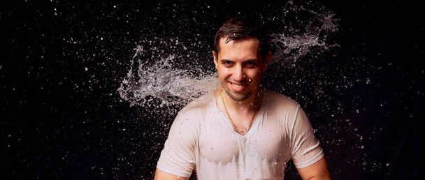 Splashes of water on the young man on dark background - Valokuva, kuva