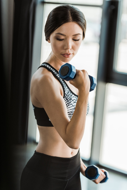 young sporty woman looking at dumbbells while working out in gym  - Photo, image