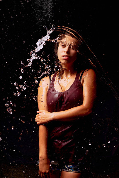 Splashes of water on the young woman on dark background - Photo, Image