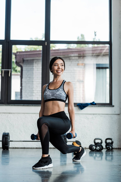 positive sportswoman doing squat exercise with dumbbells  - Foto, Imagen