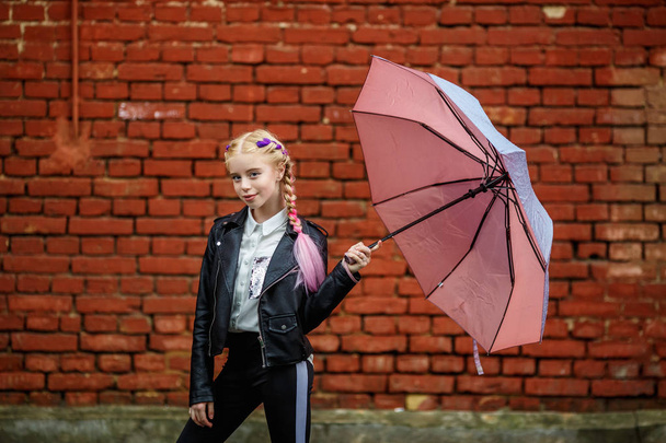 close up portrait of little beautiful stylish kid girl with an umbrella in the rain near red brick wall as background - Foto, Bild