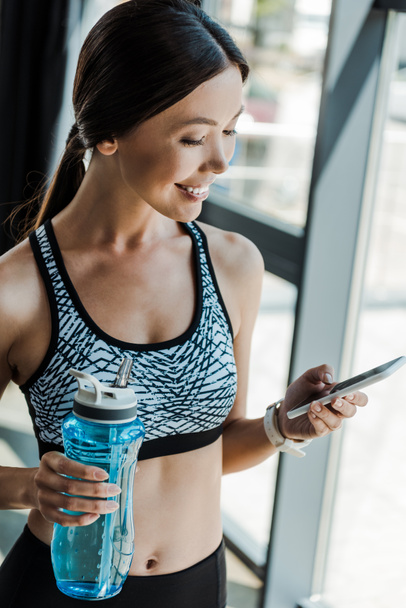 happy young woman using smartphone and holding sport bottle  - Foto, afbeelding