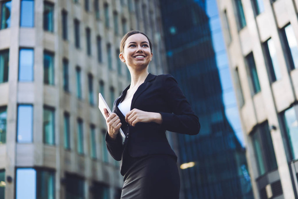 Attractive woman in formal wear looking away and enjoying good day for business deals, happy cheerful female finance manager smiling while standing on publicity area with digital tablet for chatting - Valokuva, kuva