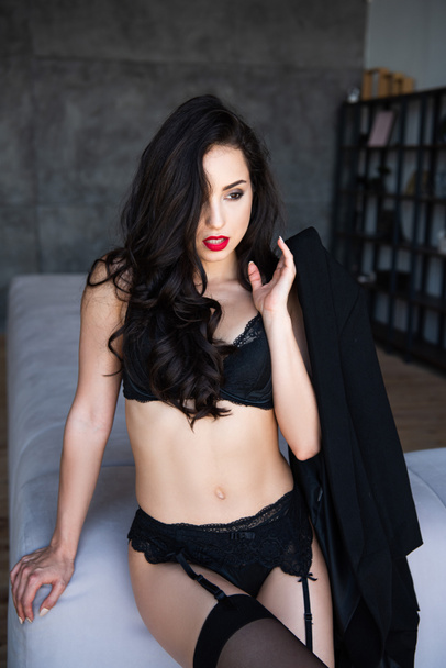  sexy girl in black underwear with jacket sitting on sofa and looking away - Zdjęcie, obraz