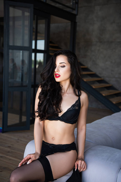  sexy girl in black underwear holding jacket while sitting on sofa with closed eyes - Foto, Imagem