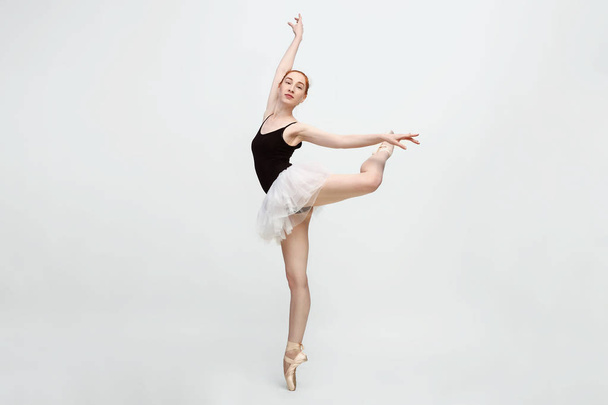 Young and incredibly beautiful ballerina is posing and dancing in a light grey studio full of light. The photo greatly reflects the incomparable beauty of a classical ballet art. Copy space - Foto, Imagem