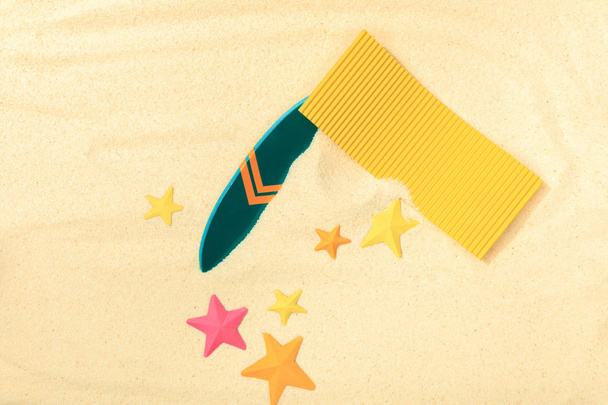 vue de dessus de la plage de papier avec planche de surf verte, serviette jaune et étoiles de mer sur sable texturé
  - Photo, image