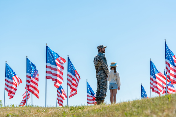 military man in uniform standing with daughter near american flags  - Foto, Imagem