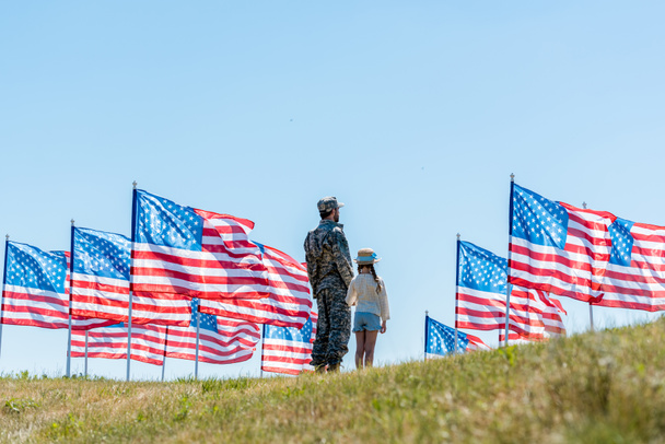 man in military uniform standing with daughter near american flags  - Photo, Image