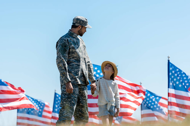 selective focus of kid holding hands with military father near american flags  - Photo, Image