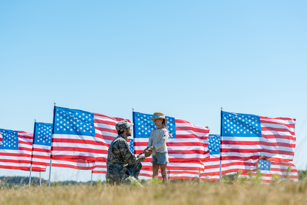 selective focus of military father holding hands with cute kid near american flags  - Фото, изображение