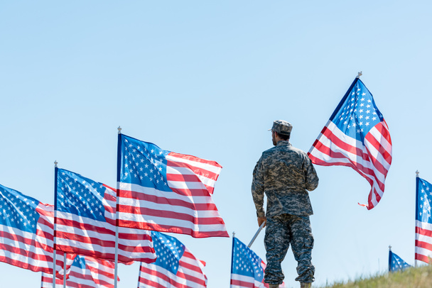 selective focus of man in military uniform and cap standing and holding american flag  - 写真・画像
