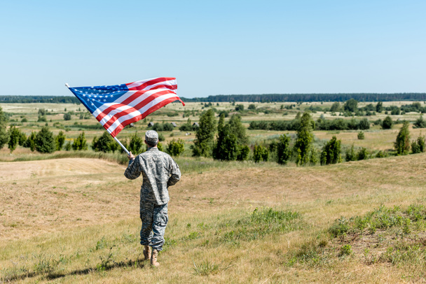 草の上に立ち、アメリカ国旗を掲げる制服姿の軍人  - 写真・画像