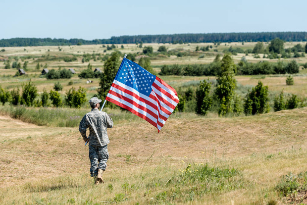 制服姿の兵士が草の上を歩き、アメリカ国旗を掲げる  - 写真・画像