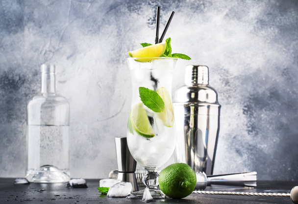 Lime caipirinha, classic Brazilian alcoholic cocktail with cane vodka cachasa, sugar syrup, lime juice and crushed ice in tall glass on gray table, bar tools, place for text - 写真・画像