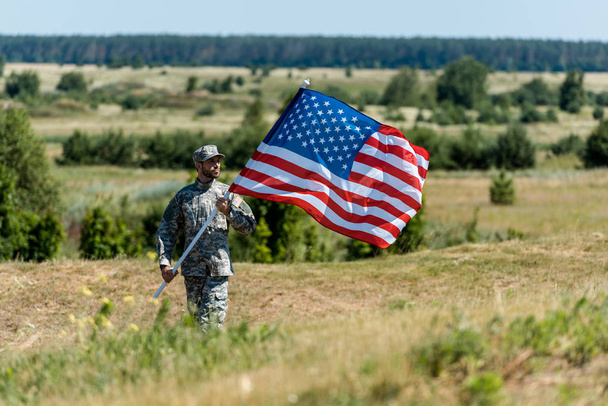 selective focus of handsome military man in uniform and cap holding american flag  - Photo, Image