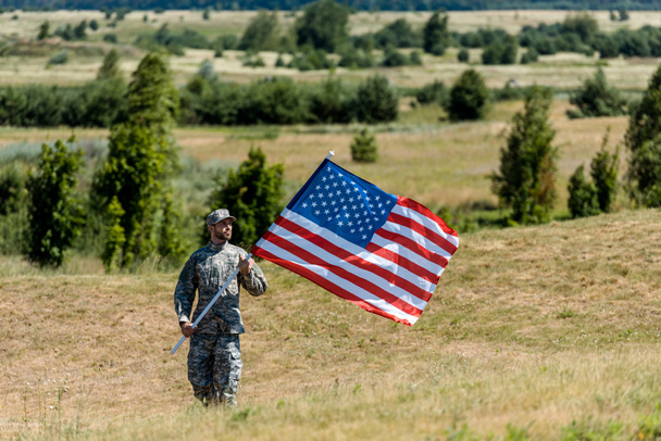 selective focus of military man in uniform and cap holding american flag in summertime  - Photo, Image