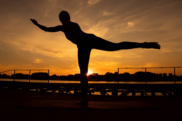 Frau praktiziert Yoga bei Sonnenuntergang. virabhadrasana / Krieger 3 Pose - Foto, Bild