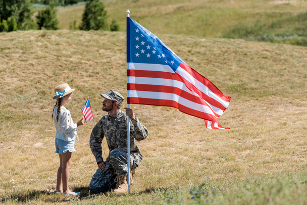 lindo niño sosteniendo bandera americana y mirando guapo militar padre
  - Foto, Imagen