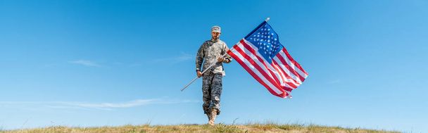 πανοραμικό πλάνο του όμορφου στρατιωτικού άντρα με στολή που κρατά την αμερικάνικη σημαία με αστέρια και ρίγες  - Φωτογραφία, εικόνα