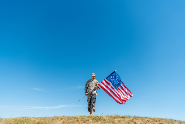 Красивый военный в форме ходит с американским флагом со звездами и полосками
  - Фото, изображение