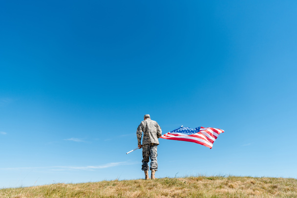 vue arrière de l'homme militaire en uniforme debout avec drapeau américain avec des étoiles et des rayures
  - Photo, image