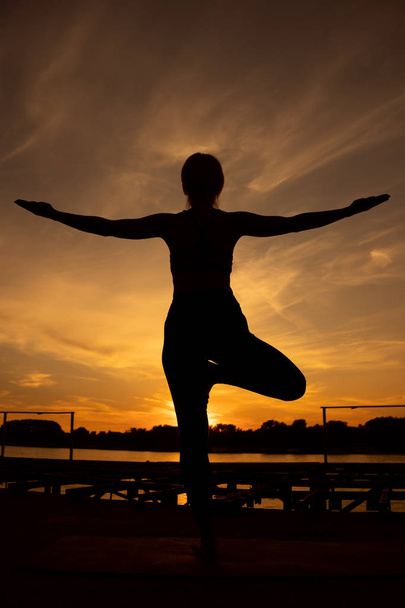 Mulher praticando ioga ao pôr do sol. Vriksasana, pose de árvore
 - Foto, Imagem