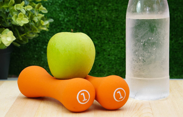 緑のリンゴと木製の背景に水のボトルとオレンジのダンベル   - 写真・画像